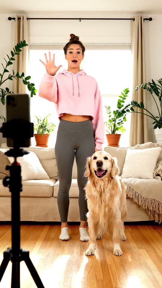 A young woman and her golden retriever perform a dance challenge together in a sunny living room