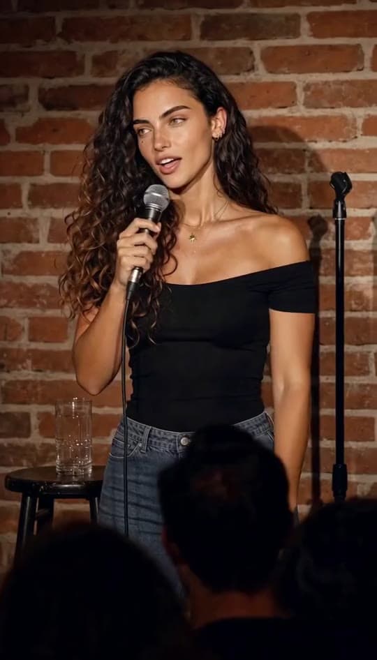 A comedian performs on a brick-wall comedy club stage and the audience laughs